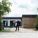Real estate agent standing outside modern house with for sale sign, featuring contemporary design.